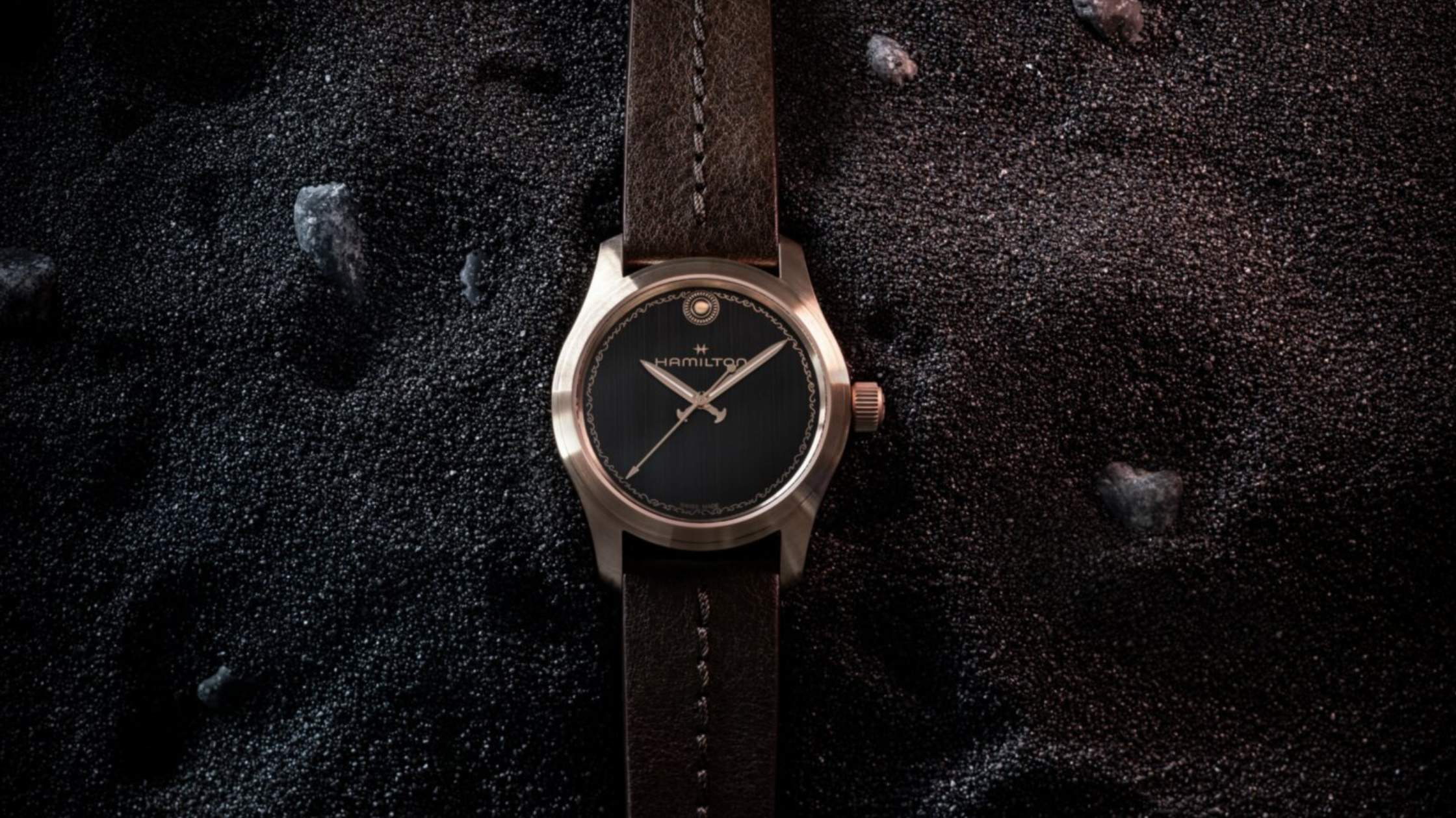 Hamilton Khaki Field Auto The Odyssey watch with a black dial and brown leather strap resting on black volcanic sand