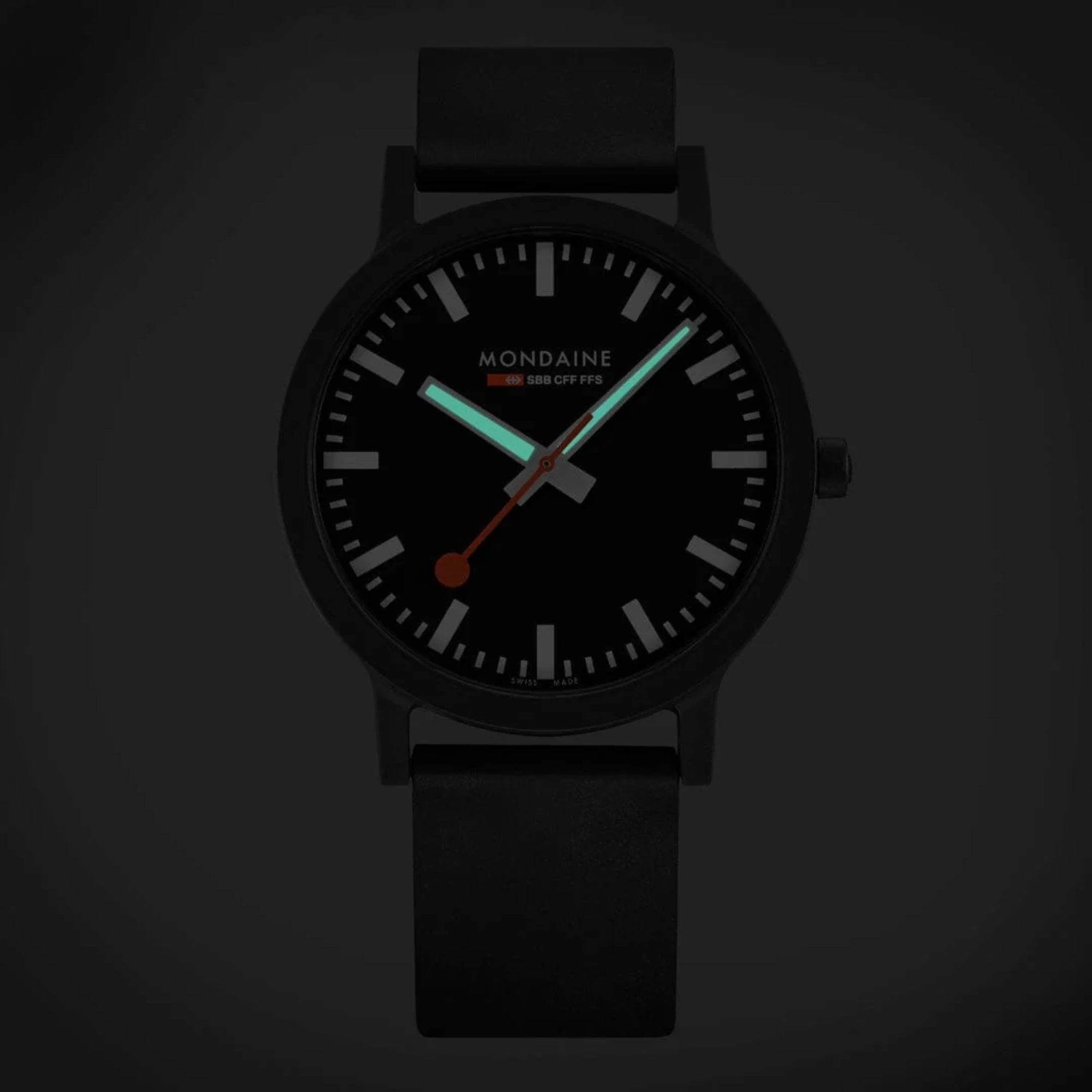 Low-light view of Mondaine Essence MS1.41120.RB Swiss Railways timepiece highlighting luminous white hands against a black analog display