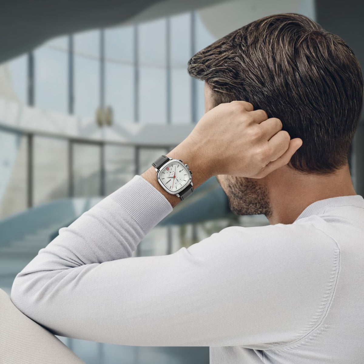Men's wristwatch with silver case and black leather strap on man's raised arm.