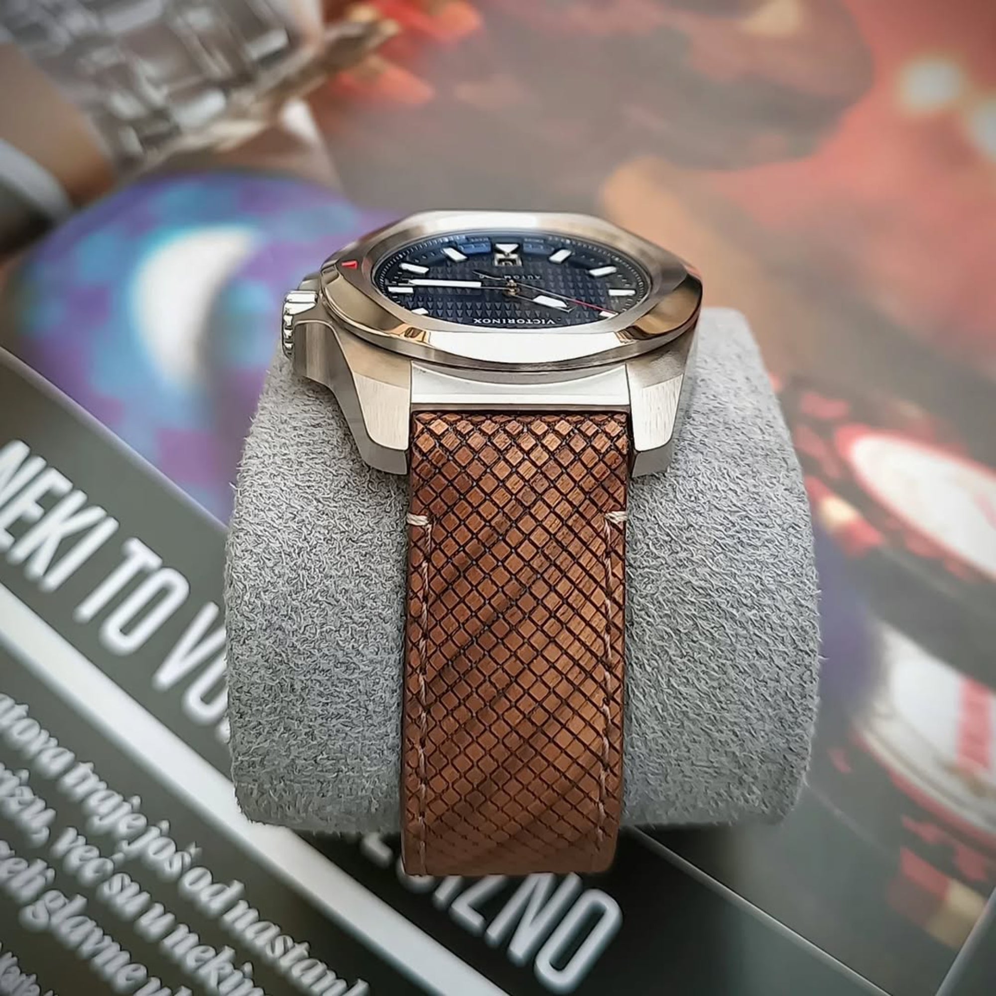 A stainless steel Victorinox I.N.O.X. watch resting on a gray display cushion and featuring a textured brown cross-hatch strap