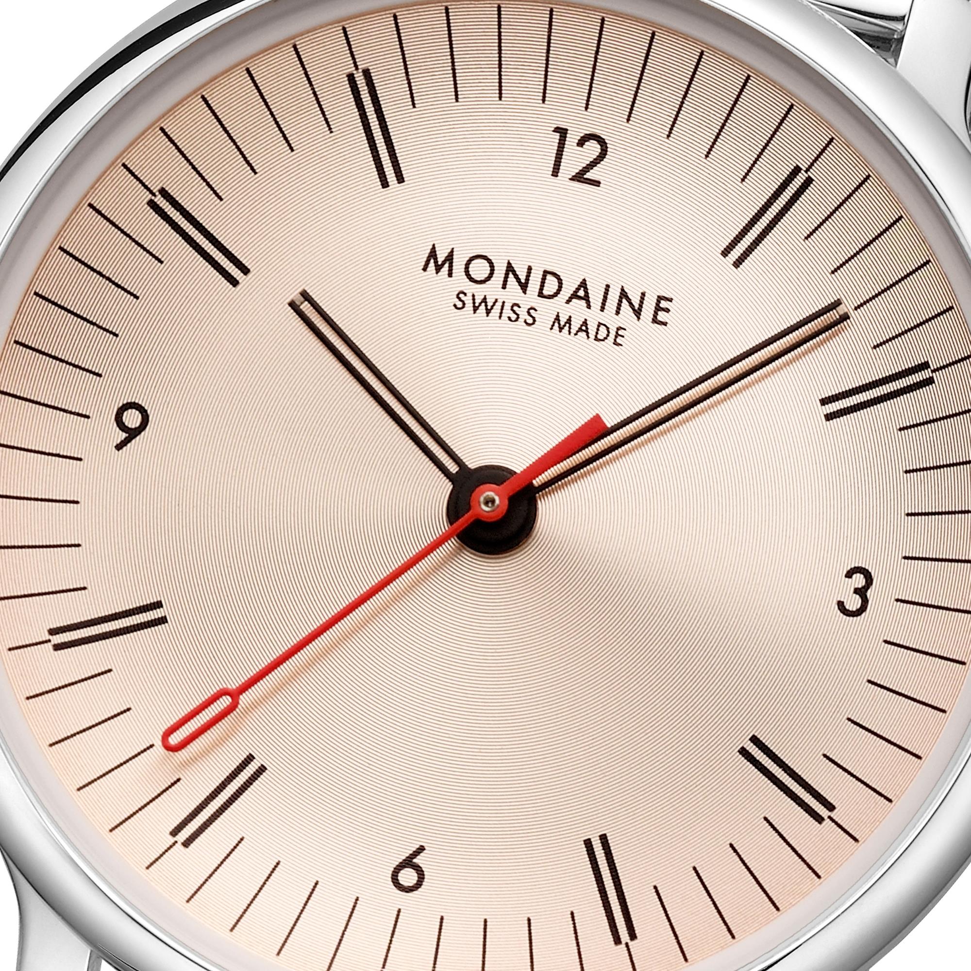 Close-up of the rose gold watch face, detailing the "MONDAINE SWISS MADE" lettering, the black baton hands, and the iconic red second hand with its circular tip