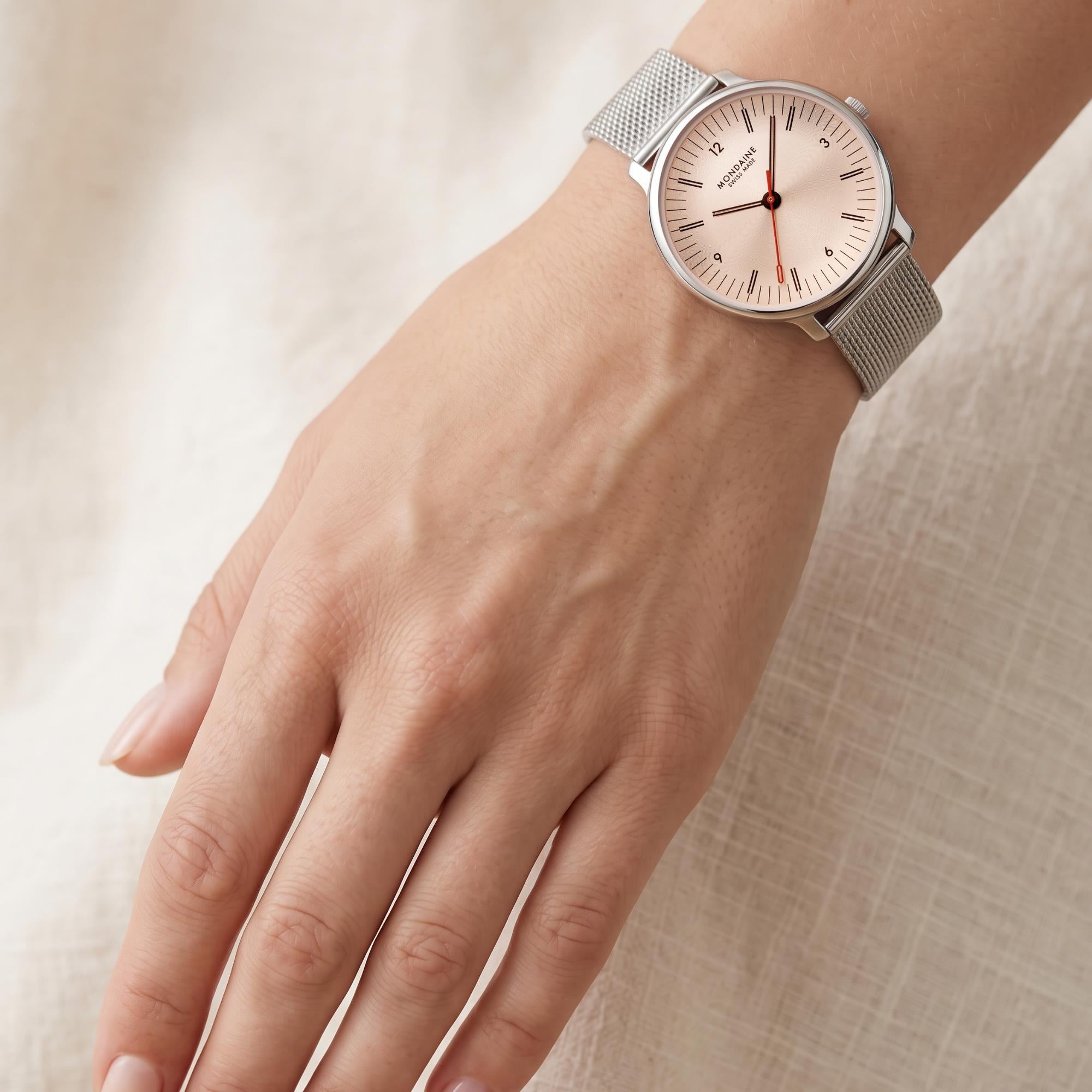 An overhead top-down wrist shot showing the full drape of the silver-tone mesh bracelet and how the 33mm rose gold watch face sits on a woman's wrist