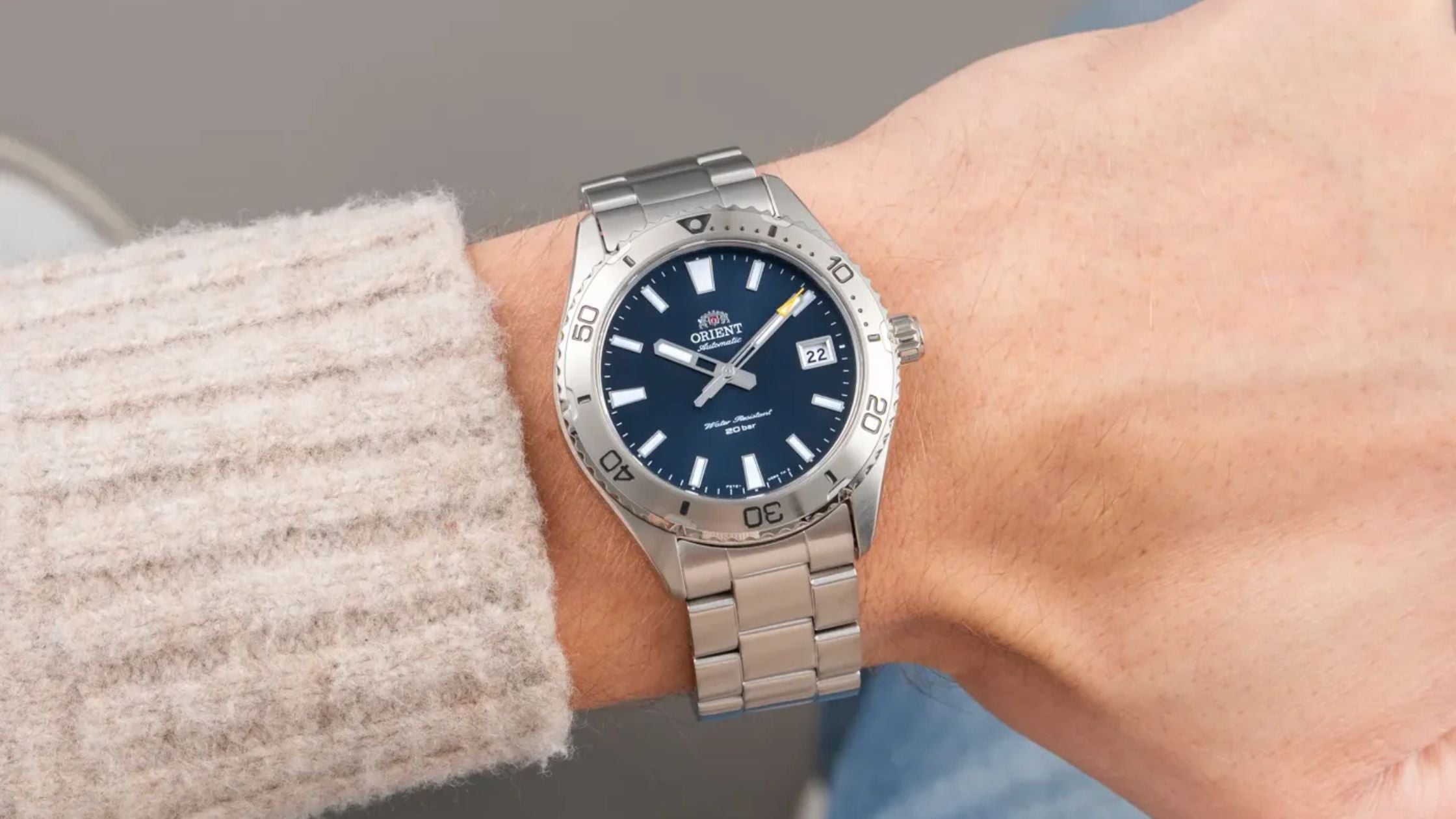 Close-up of an Orient automatic dive watch with a blue dial and stainless steel bracelet on a wrist