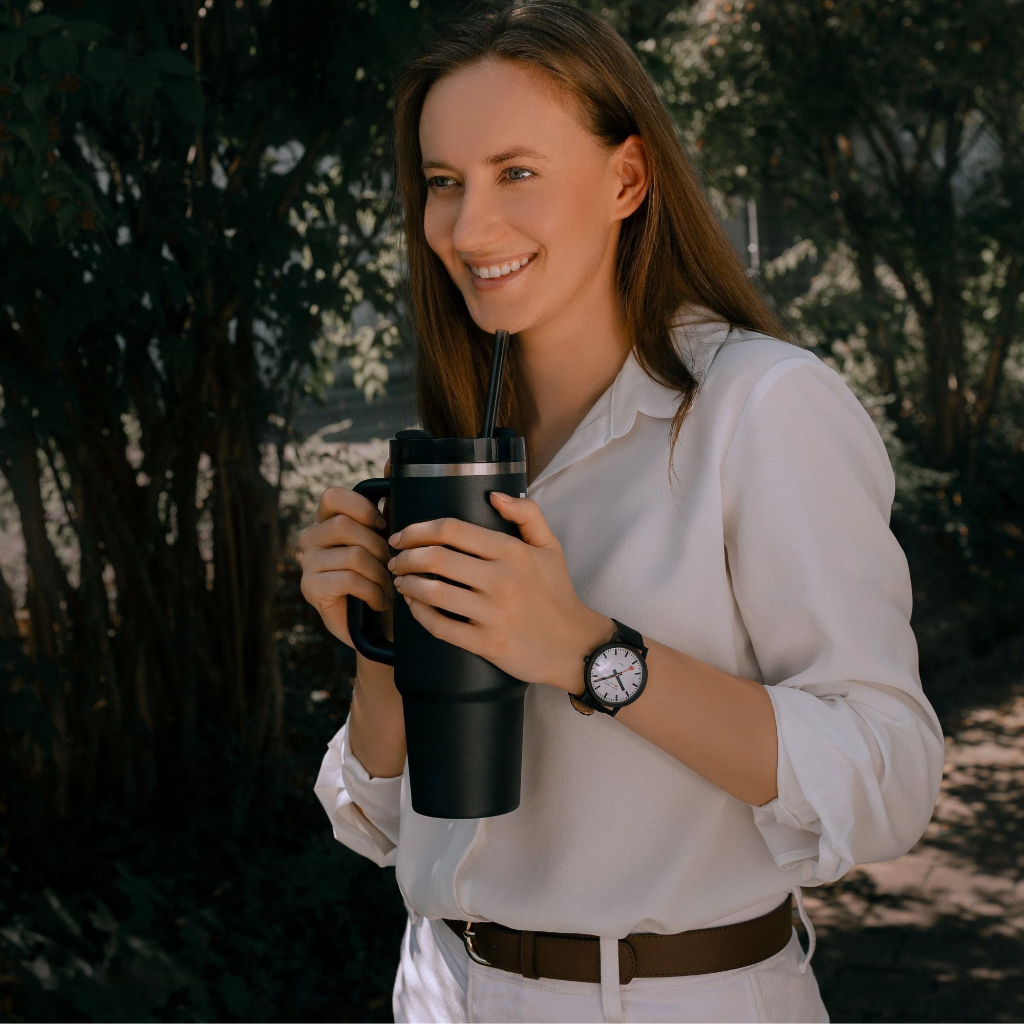 Mondaine Essence MS1.41910.LB 41mm sustainable solar watch worn on a womans wrist while holding a dark travel tumbler outdoors