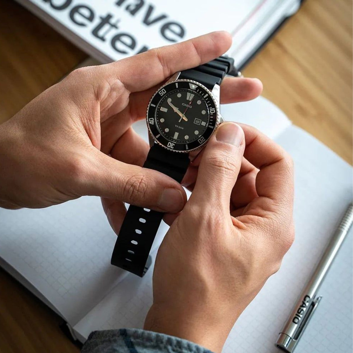 Casio Marlin MDV-107-1A1VEF close-up showing the watch being adjusted over a notebook, highlighting its crown and strap details