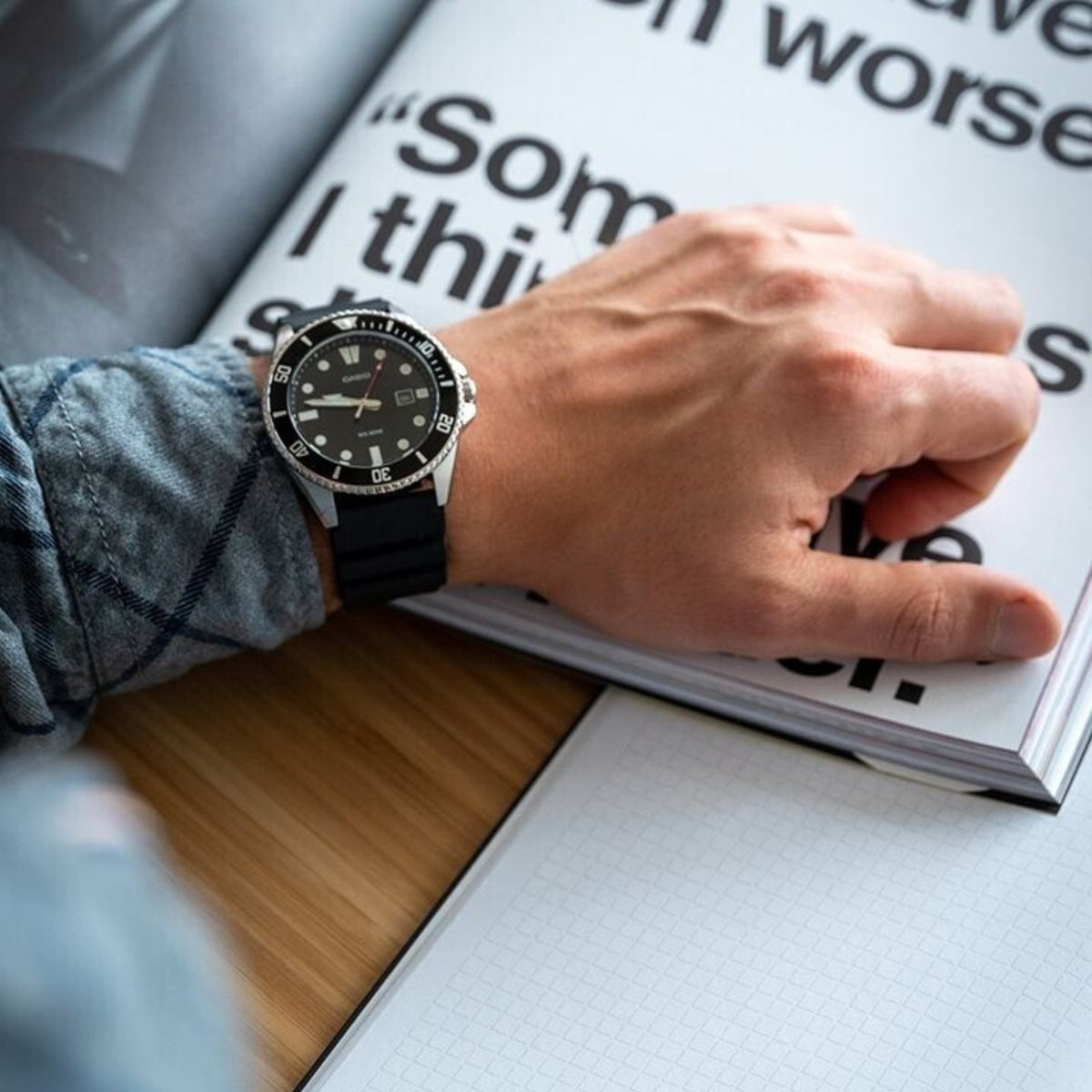 Casio Marlin MDV-107-1A1VEF on a person's wrist over an open book, showcasing the rugged black resin strap and steel case