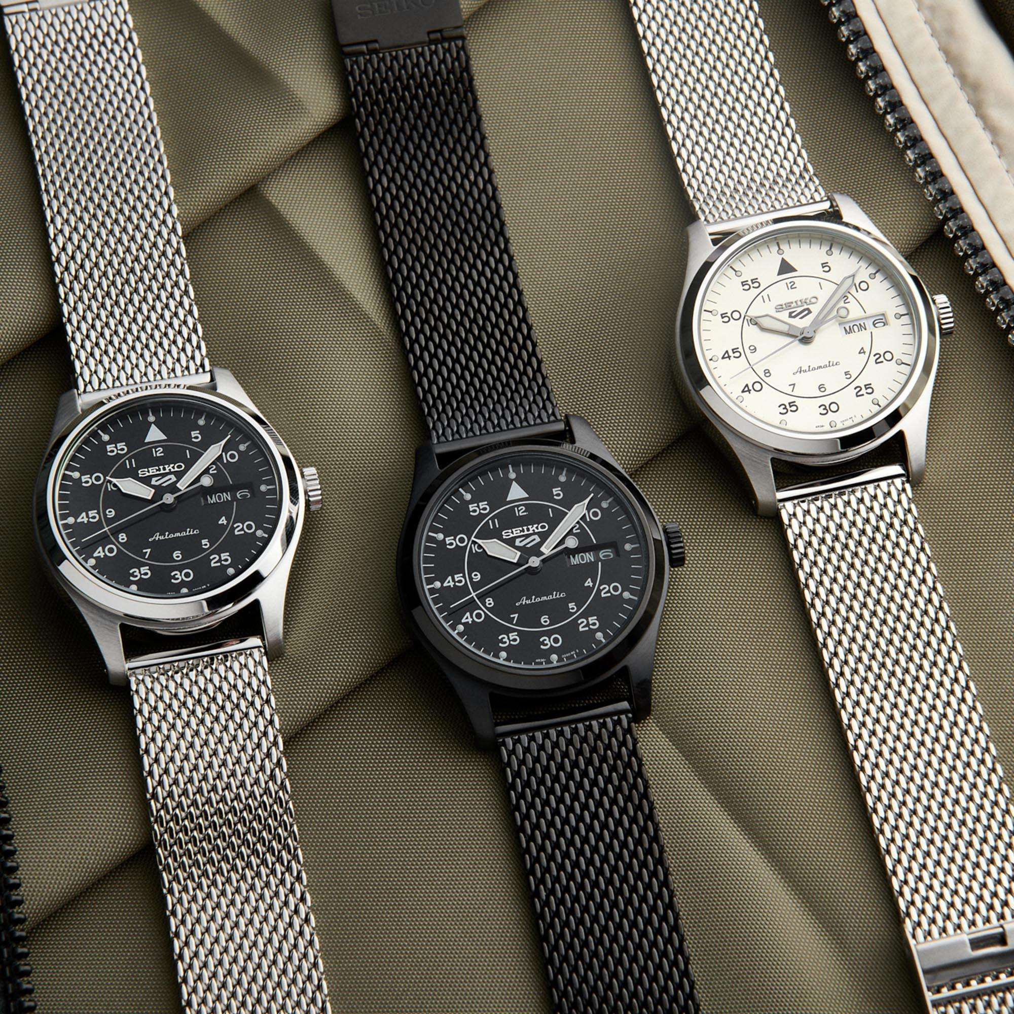 Three Seiko watches with different mesh straps on a textured surface