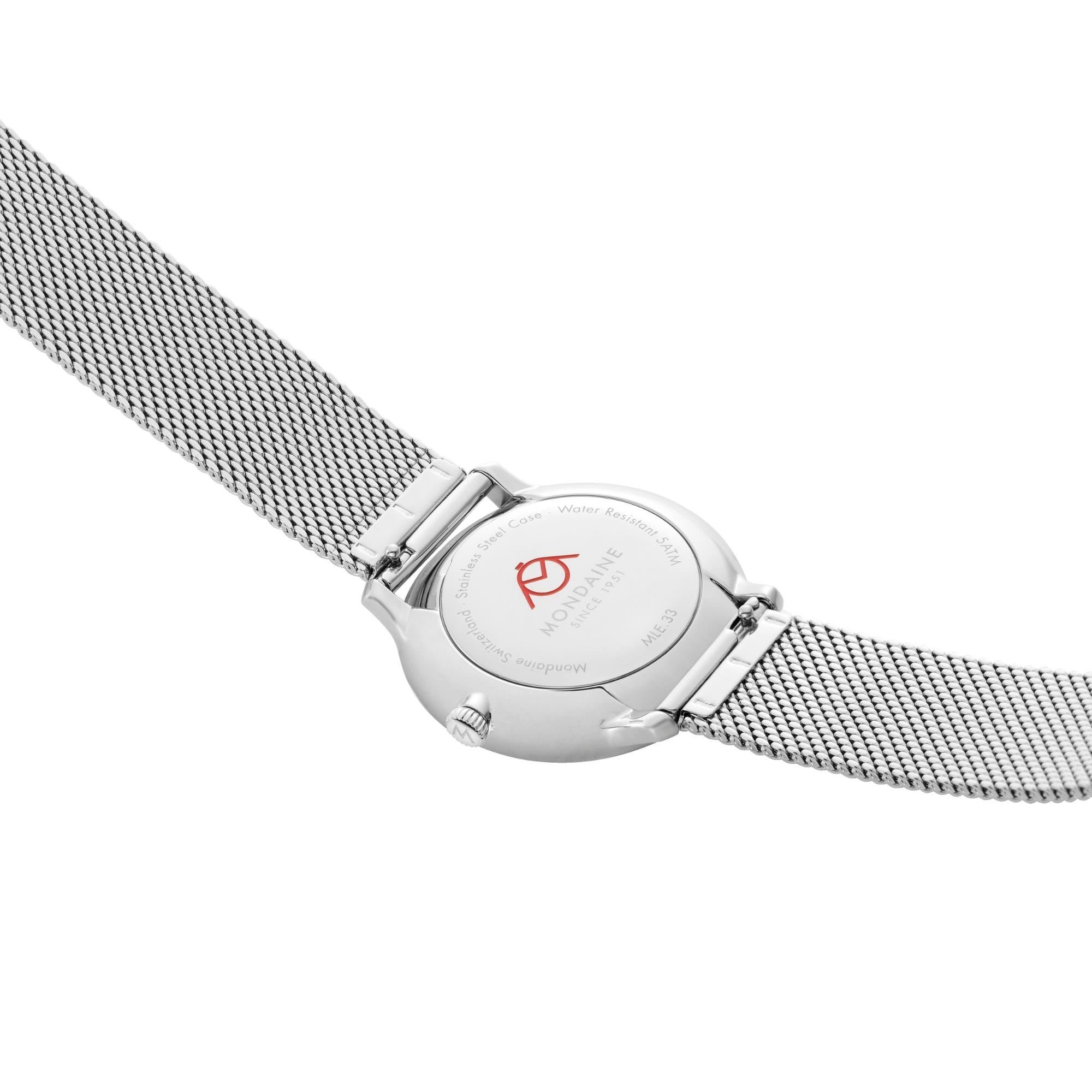 The polished stainless steel caseback of Mondaine Doppio watch, showing an engraved red logo at the center and the connecting ends of the silver mesh strap