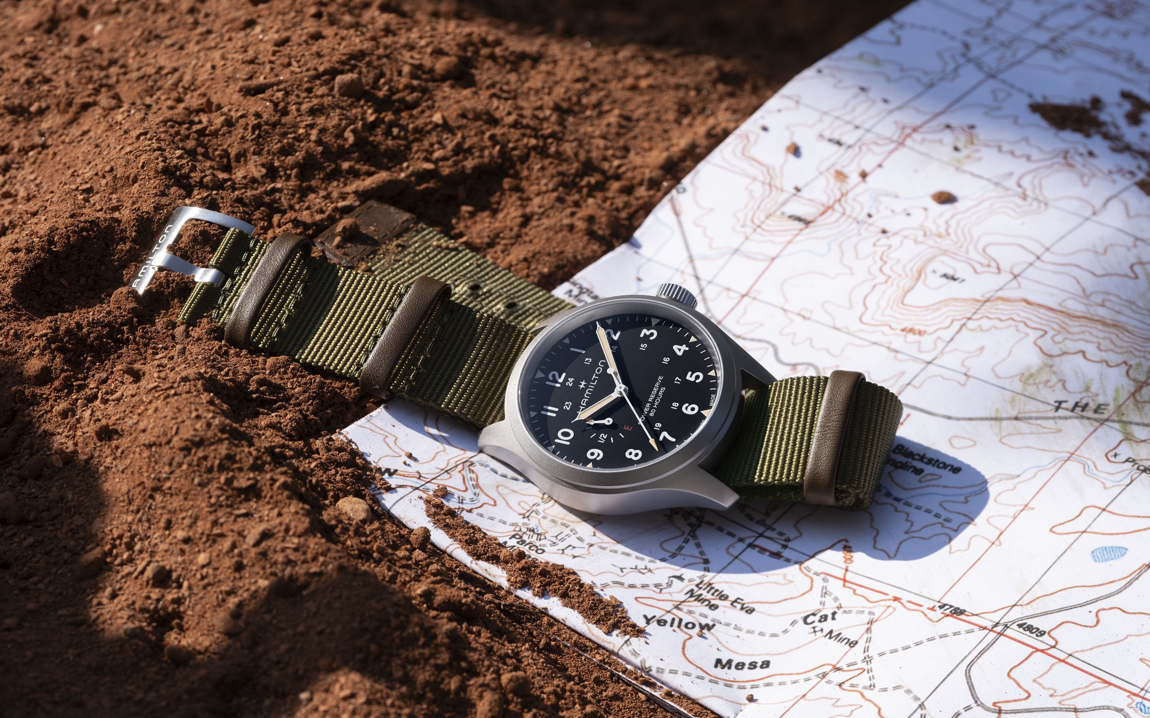 Hamilton Khaki Field Mechanical Power Reserve watch with black dial on topographic map and red soil